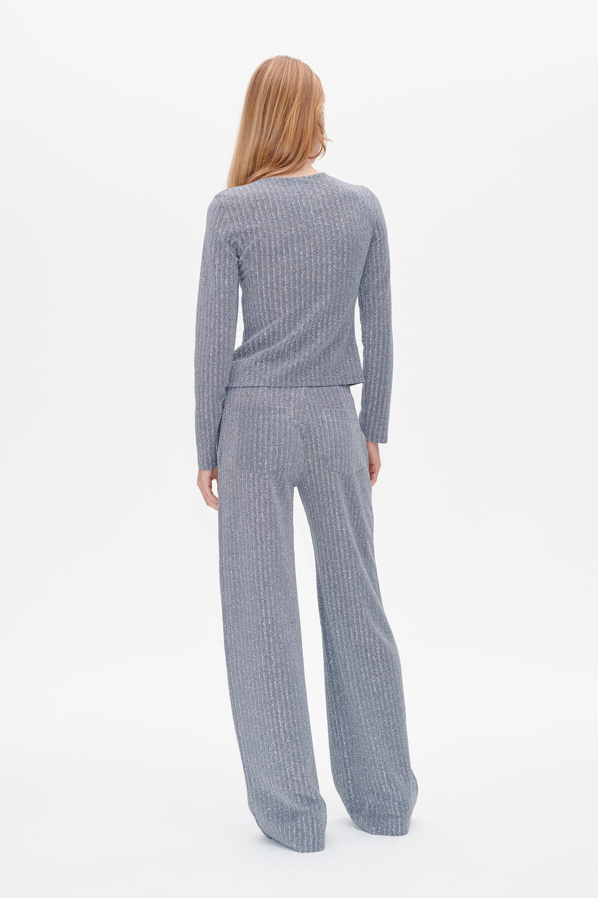 Rückenansicht eines Models, das ein graues, langärmeliges, geripptes Top und eine passende, weite Hose mit dezenten vertikalen Sprenkeln trägt.