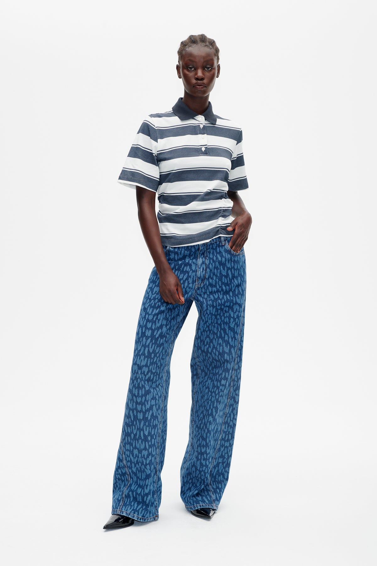 Model trägt ein marineblau-weiß gestreiftes kurzärmliges Poloshirt und eine weit geschnittene blau gemusterte Jeans, von vorne.