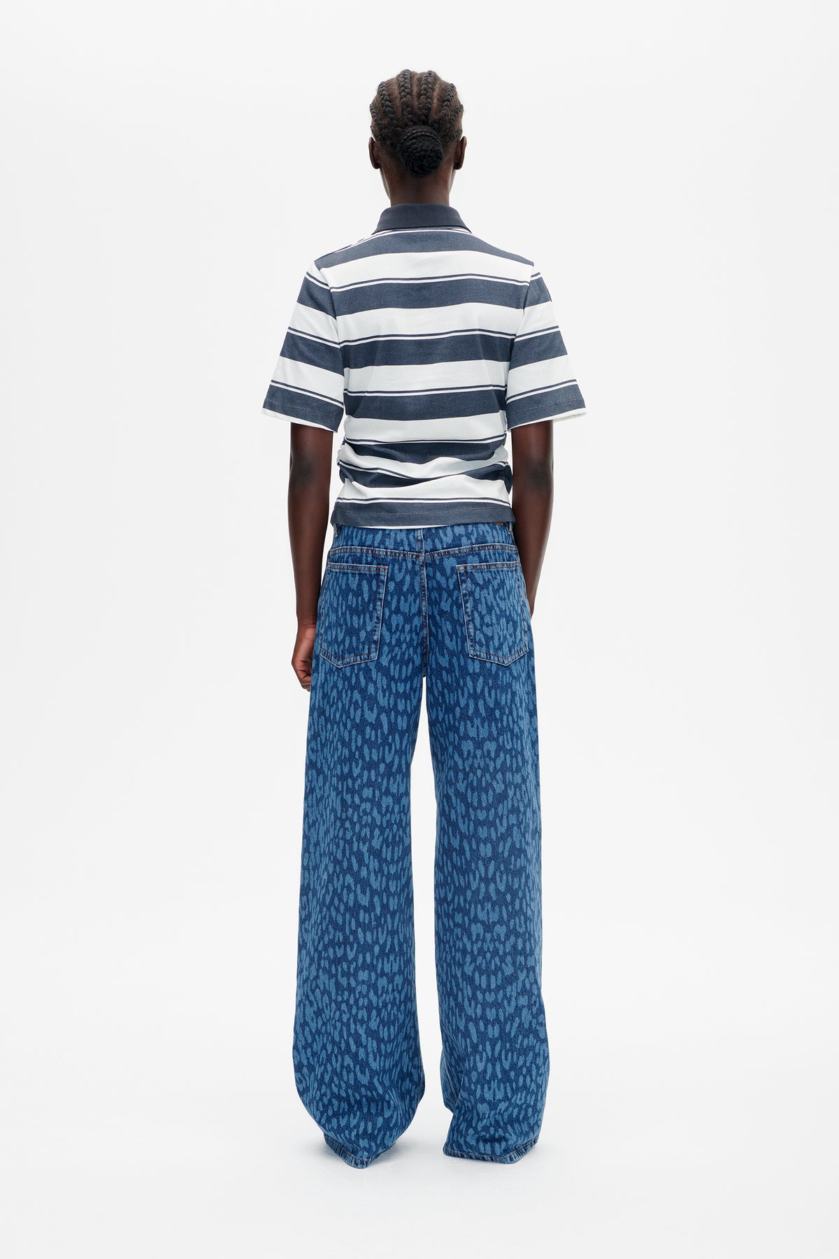 Rückenansicht eines Models, das ein kurzärmeliges, marineblau-weiß gestreiftes Hemd mit Kragen und eine weit geschnittene, blau gemusterte Jeans trägt.