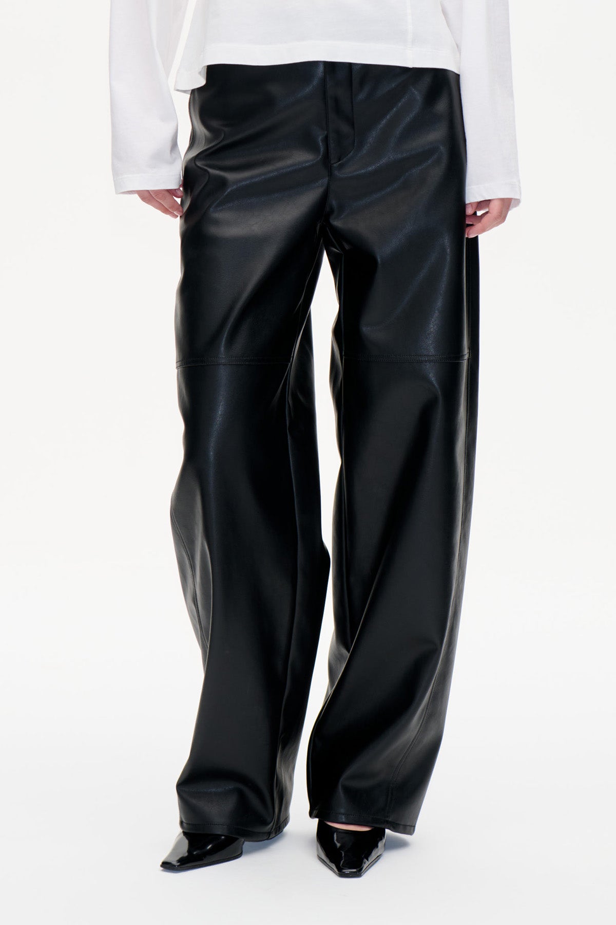 Detail der Vorderseite einer glänzenden schwarzen Hose mit weitem Bein und horizontalen Nähten am Knie, gestylt mit einem weißen Langarmtop.