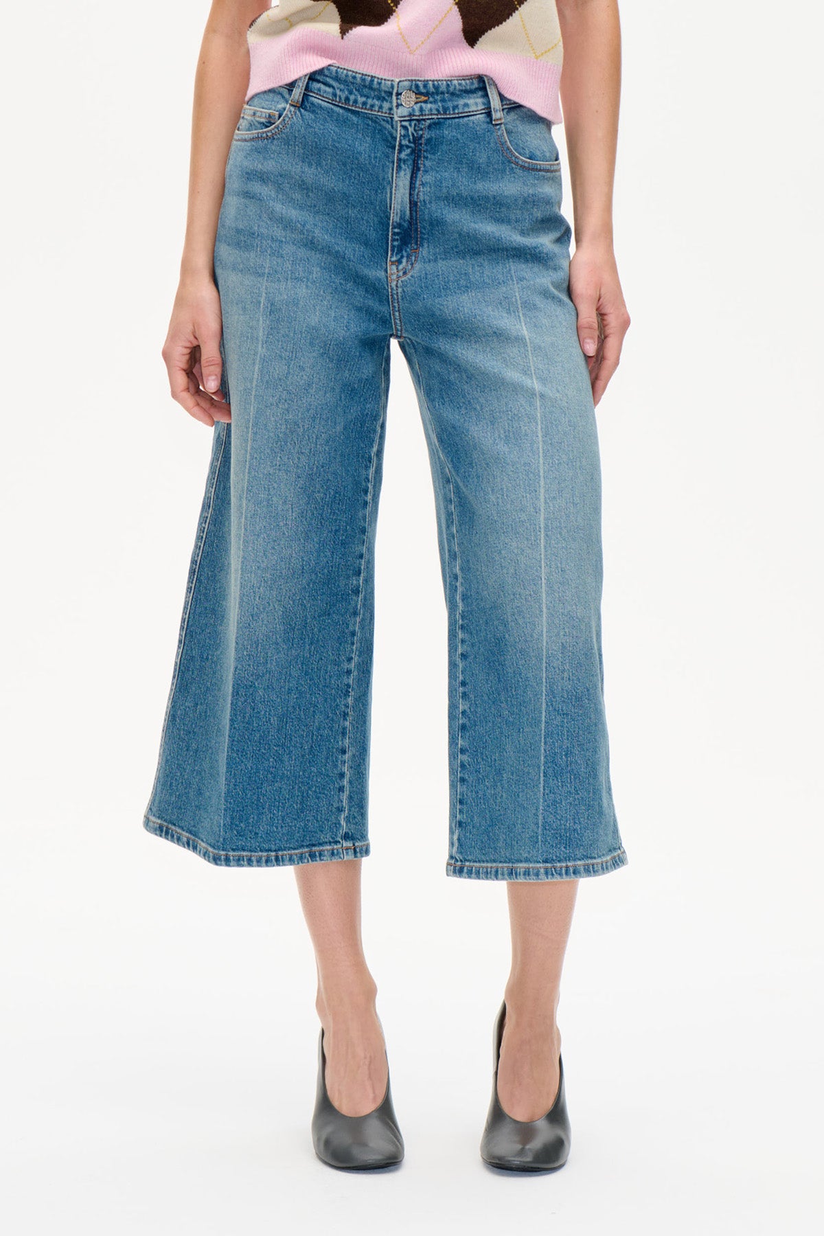 Vorderansicht einer weit geschnittenen, verkürzten blauen Jeans mit ausgewaschenem Finish, getragen mit einem rosé- und cremefarben gemusterten Stricktop.