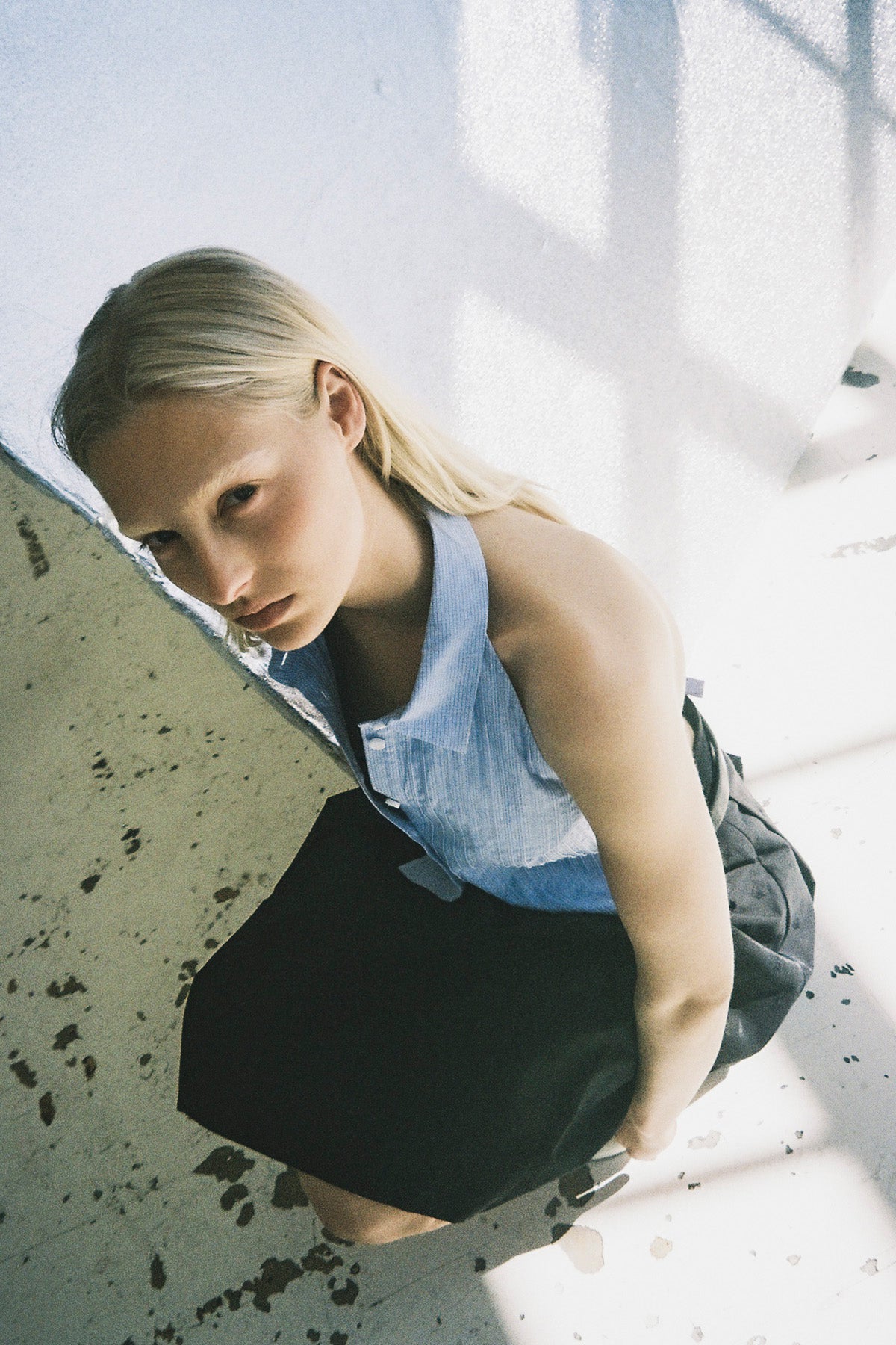 Von oben fotografiertes Model, das sich nach vorne beugt und ein hellblaues ärmelloses Top mit Kragen und durchgehender Knopfleiste sowie einen schwarzen Rock trägt.