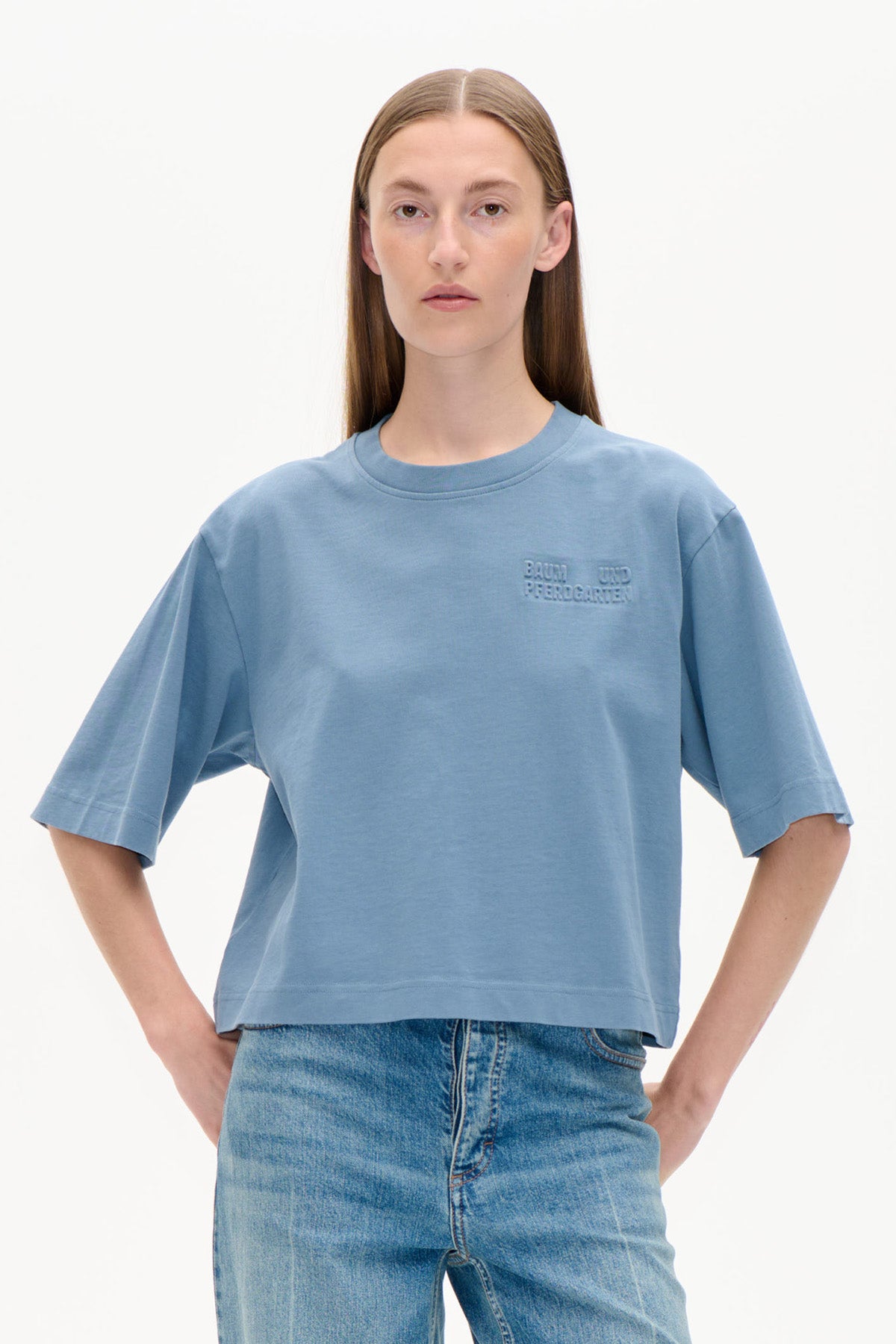 Vorderansicht eines Models in einem hellblauen oversized Kurzarm-T-Shirt mit geprägtem Brustlogo und blauen Jeans.