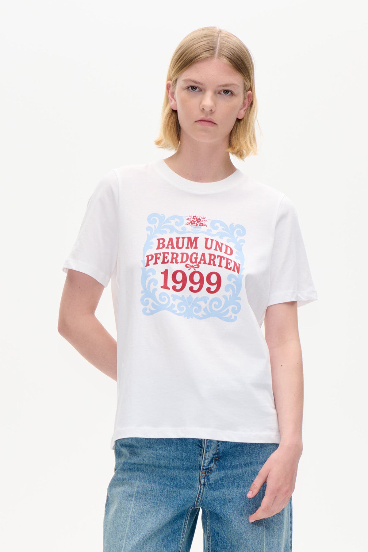 Weißes Kurzarm-T-Shirt mit blauem Ornamentrahmen und einer roten Baum und Pferdgarten 1999-Grafik, Vorderansicht.