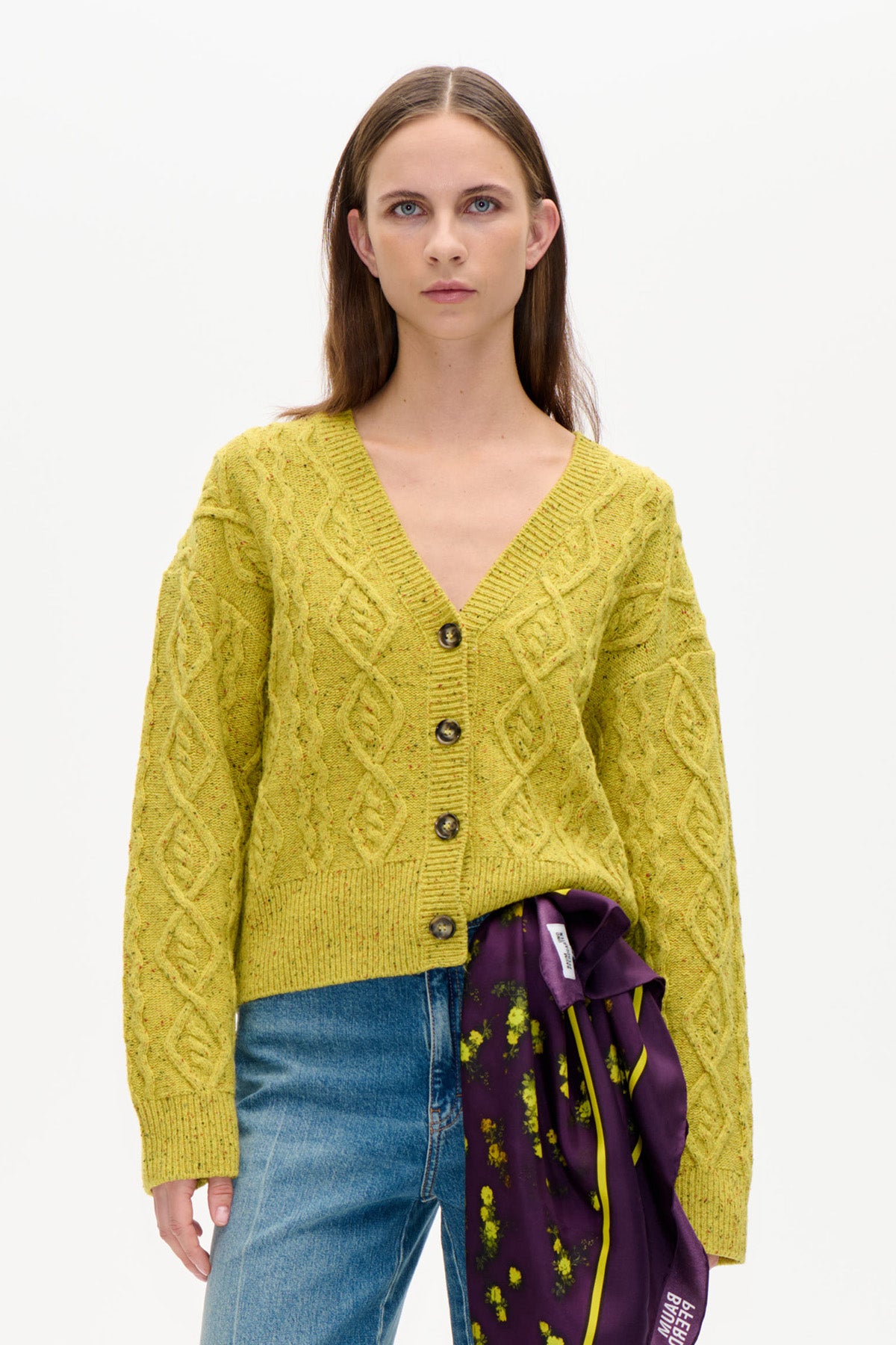 Vorderansicht einer limonengelben Zopfmusterstrickjacke mit V-Ausschnitt, langen Ärmeln und dunklen Knöpfen, gestylt mit blauen denim-Jeans.