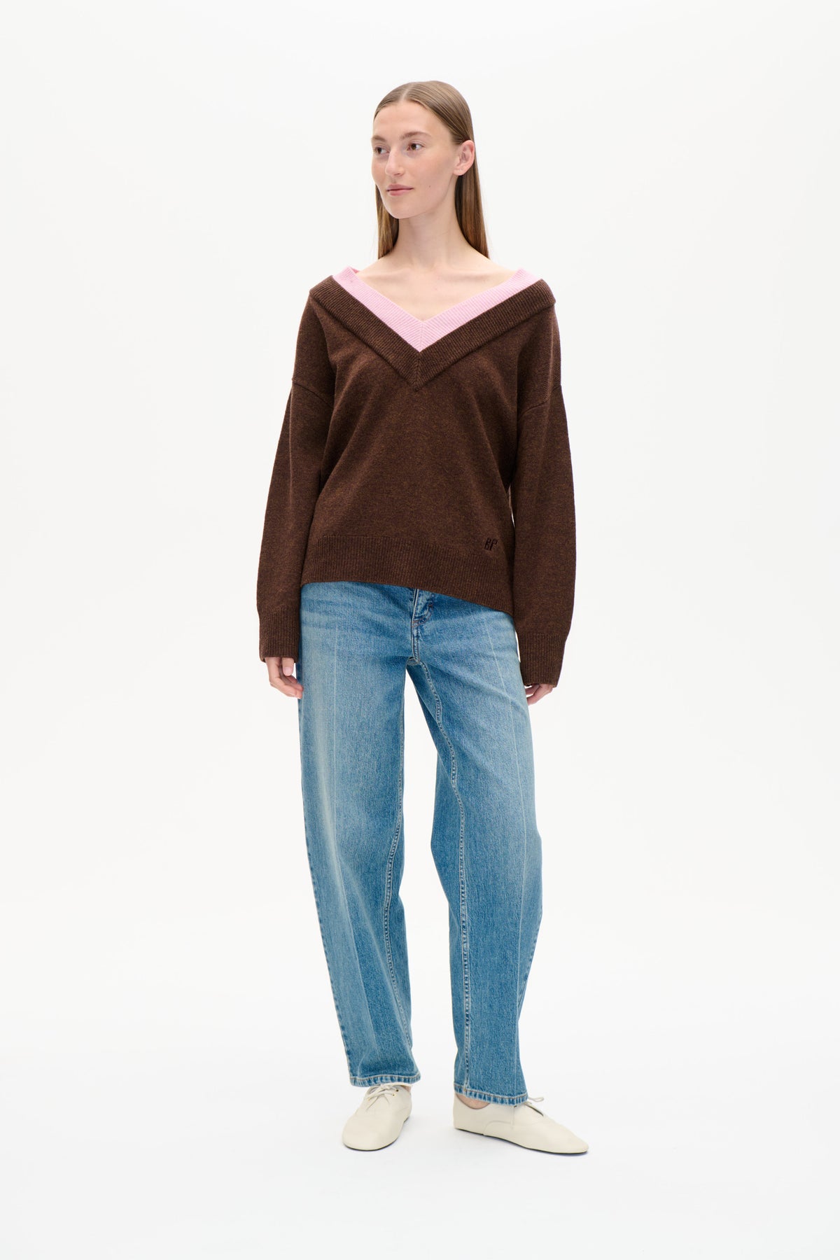 Vorderansicht eines braunen Strickpullovers mit breitem pinkem V-Ausschnitt, kombiniert mit hellblauen Jeans.