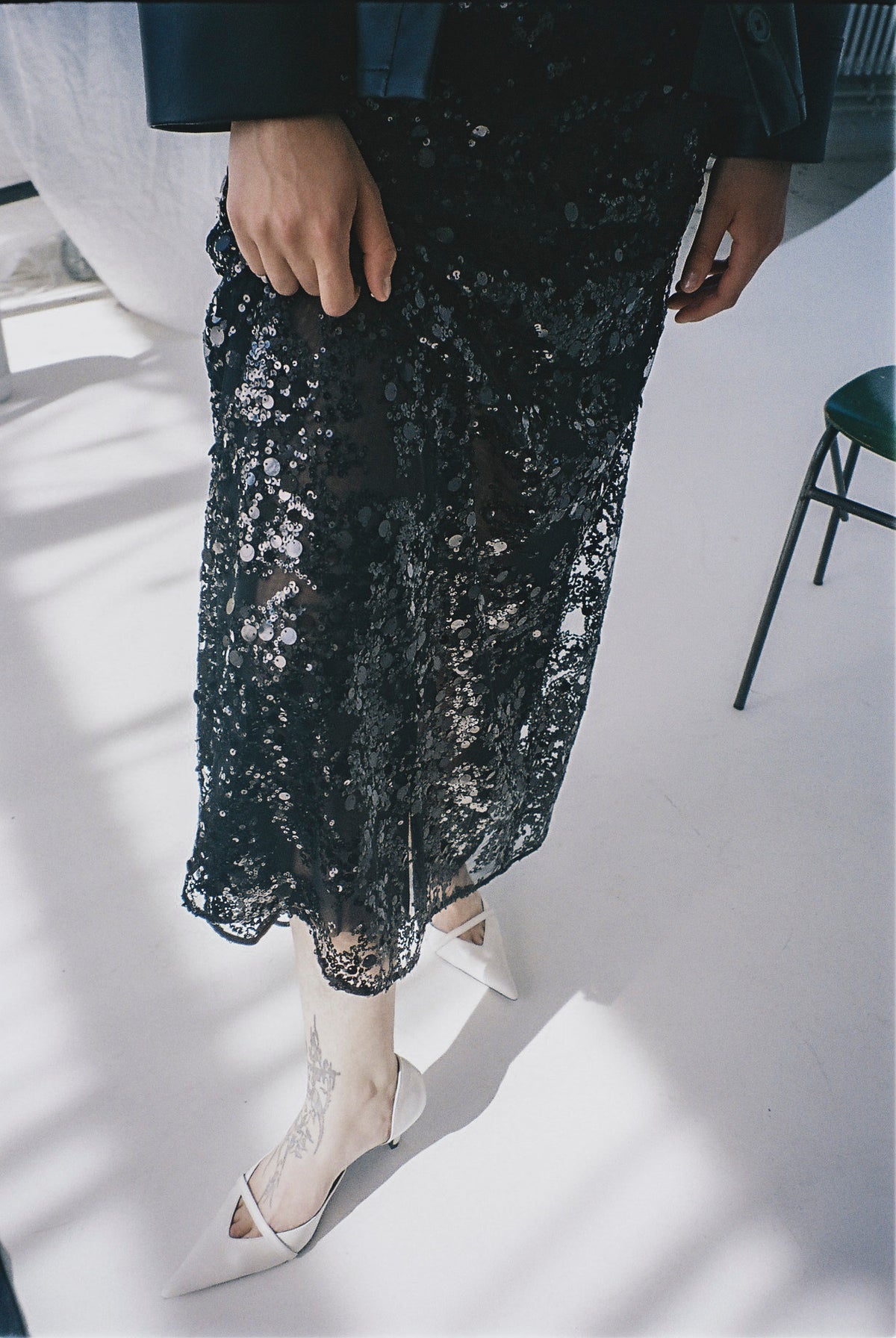Kampagnen-Nahaufnahme eines Models in einem schwarzen, transparenten Rock mit silbernen Pailletten und weißen, spitzen High Heels.
