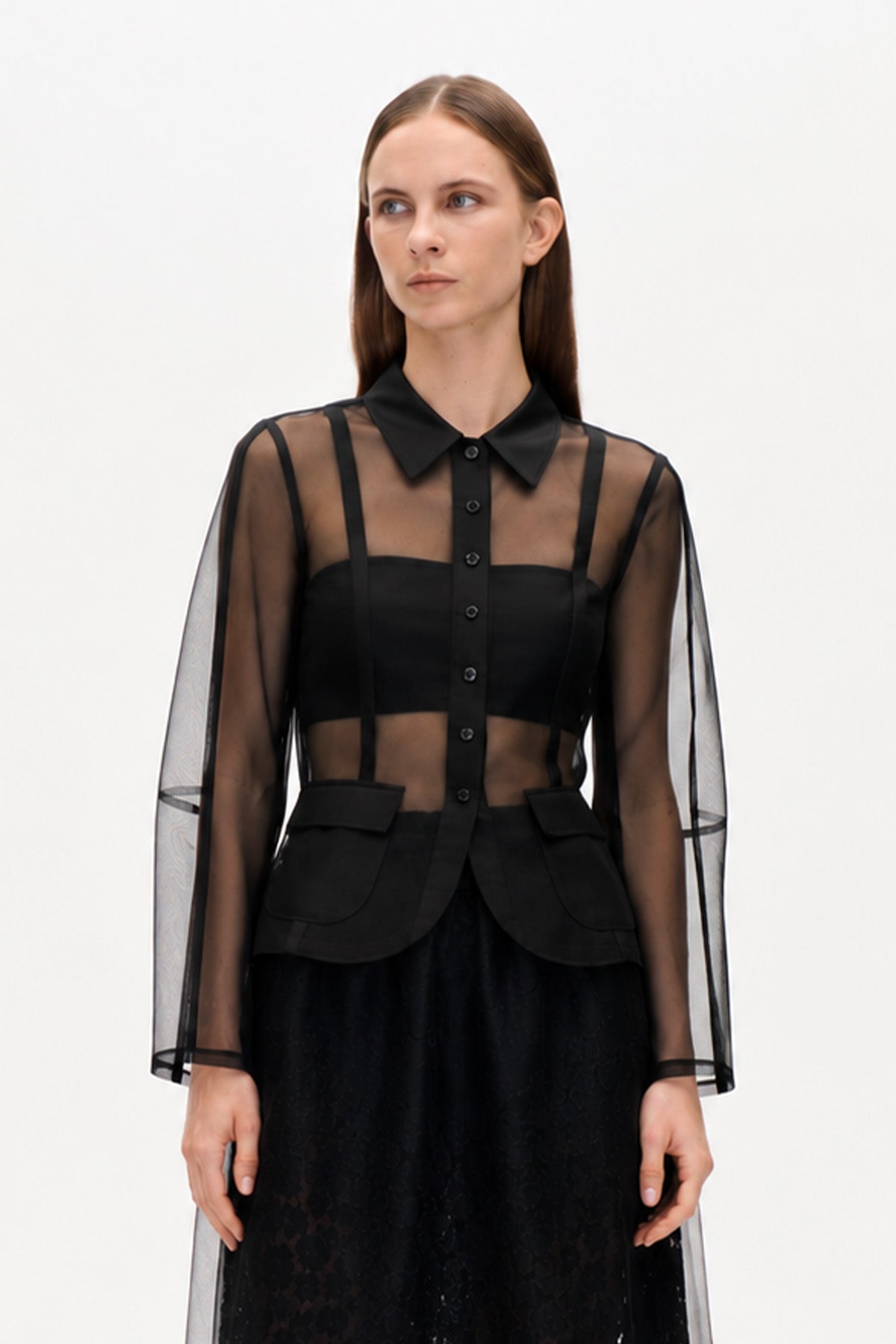 Schwarze, transparente Bluse mit langen Ärmeln, einer durchgehenden Knopfleiste, spitzem Kragen, blickdichter Blende und Klappentaschen, von vorne.