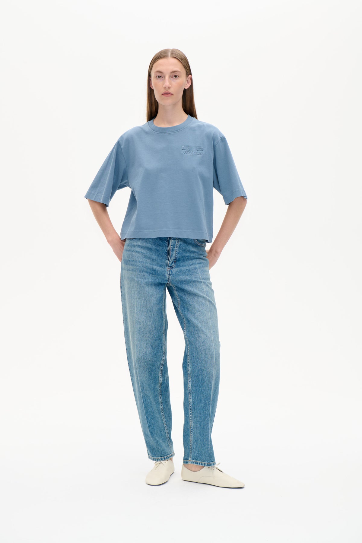 Vorderansicht eines Models in einem oversized blauen Rundhals-T-Shirt mit ellenbogenlangen Ärmeln und einem tonalen Logo auf der Brust, kombiniert mit Jeans.