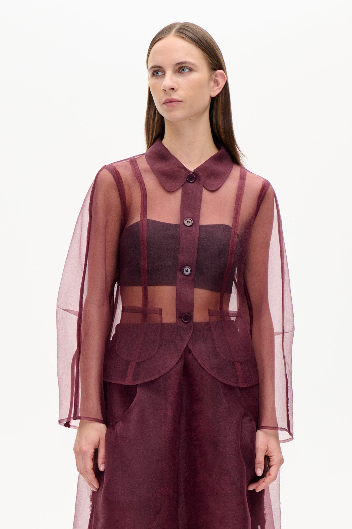 Vorderansicht einer durchscheinenden, burgunderfarbenen Bluse mit Knopfleiste, abgerundetem Kragen und weiten Ärmeln, getragen über einem dunklen Bandeau-Top und einer passenden Hose.