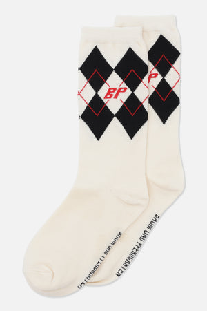 Paar cremefarbener Socken in Crew-Länge mit schwarzen Argyle-Rauten, jeweils dünn rot umrandet, und einem roten Monogramm am Bündchen.