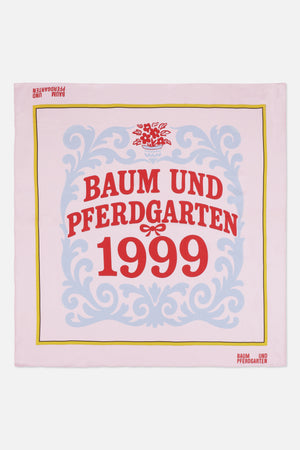 Quadratisches Tuch in blassrosa mit blauem ornamentalen Rankenmuster, gelbem Rand und rotem Schriftzug Baum und Pferdgarten 1999